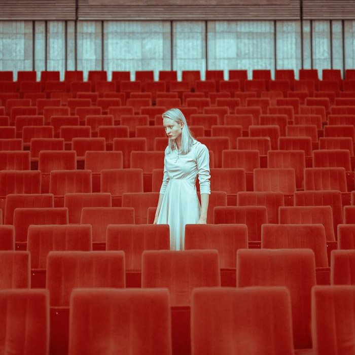 A femal model in white posing between red theatre seats by v - fashion photography style