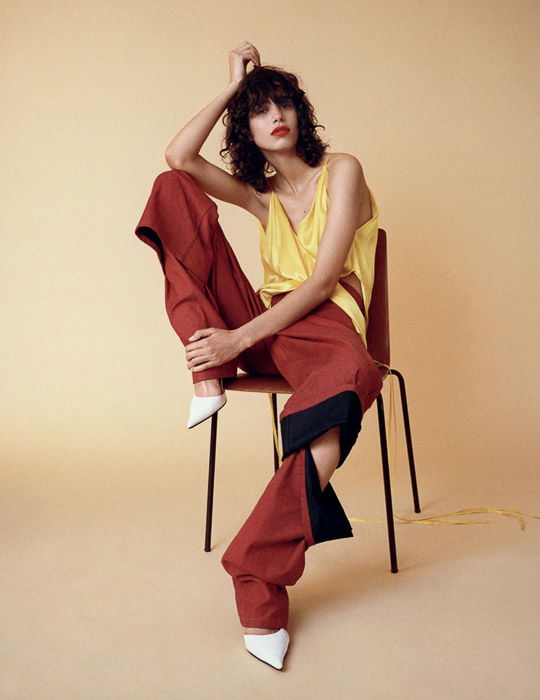 A female model posing on a chair against a pale yellow background - fashion photo inspiration 