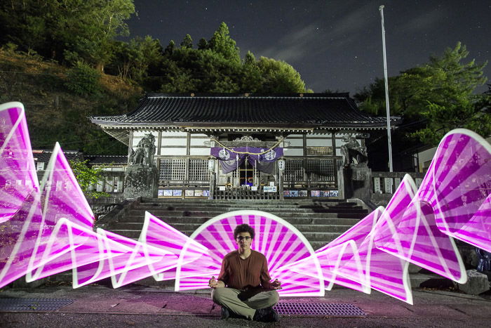 A creative holiday photography portarit of a man sitting cross legged with pink light painting shapes surrounding him