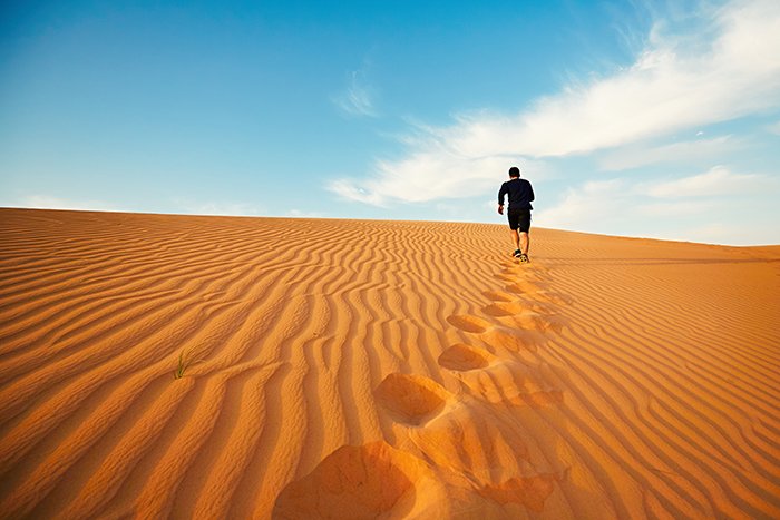 Young man is running to the top of dune in desert.