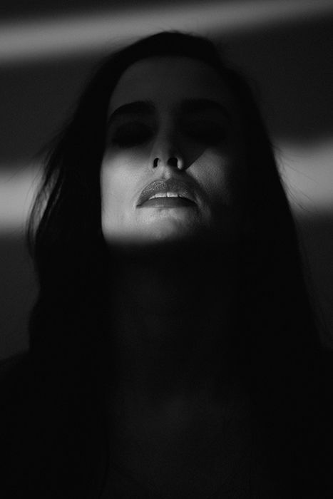 Film noir photography portrait of a female model whose eyes are naturally concealed by dark shadows to create a spooky and intriguing atmosphere.