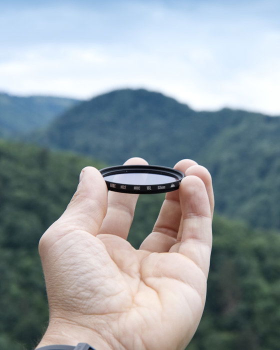 A hand holding a UV filter against a stunning landscape - photography business equipment