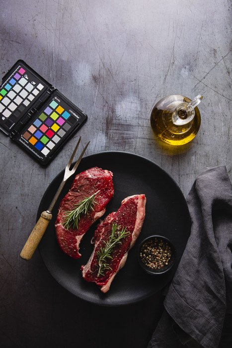 Food photography still life including a plate of raw meat, olive oil and color checker - photography business equipment