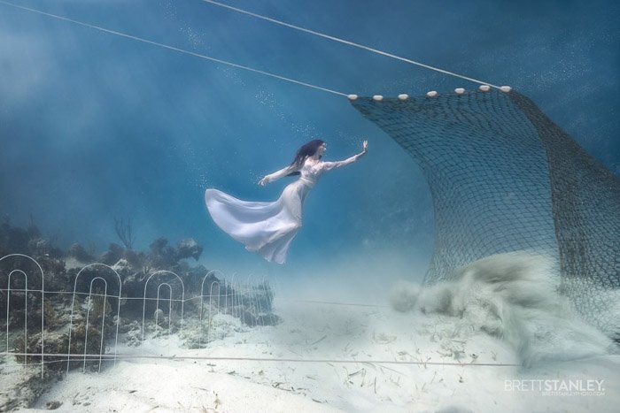 Dreamy underwater portrait of a female model swimming towards a net