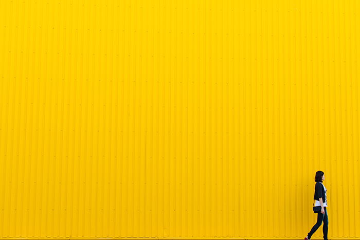 colorful portrait of a female model walking passed a bright yellow wall - using vibrant colors in photography