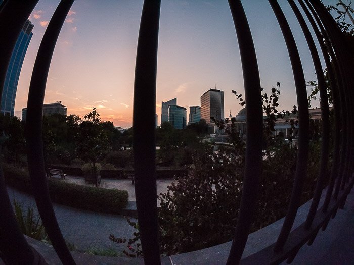 A cityscape shot through fence railings in low light, demonstrating lens distortion from using a fisheye lens