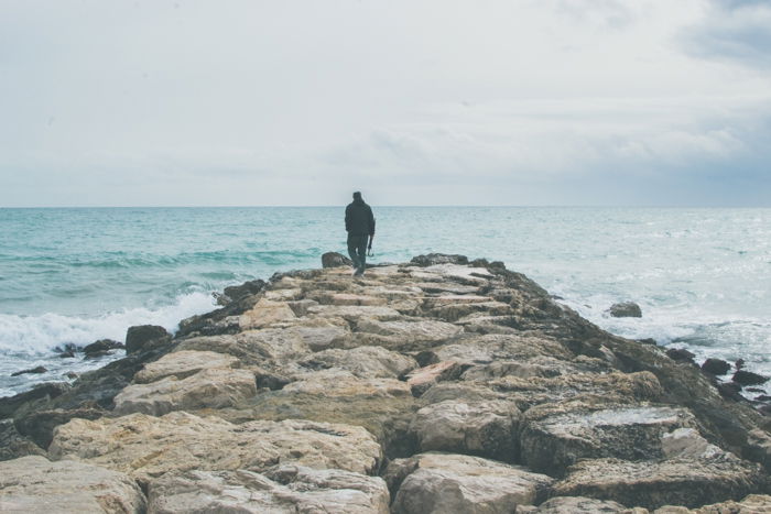 bright and airy shot of a man walking towards the sea on a rocky pier - focal point photography 