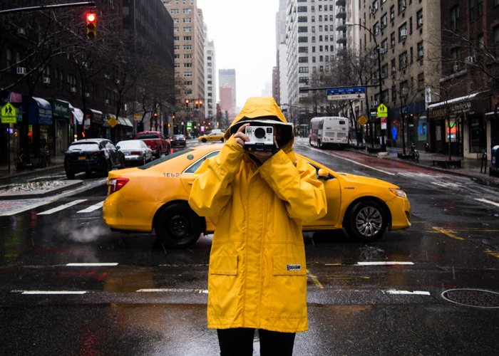A photographer in a yellow mac shooting outdoors in front of a yellow taxi cab in the rain - cool spring photos