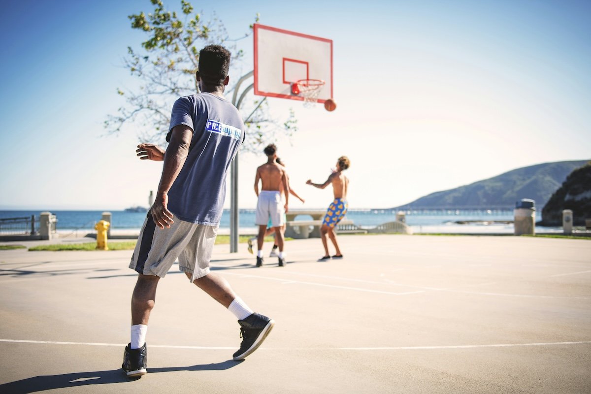 A person who just shot a ball on an outdoor court with two players waiting for the rebound as an example of basketball photography