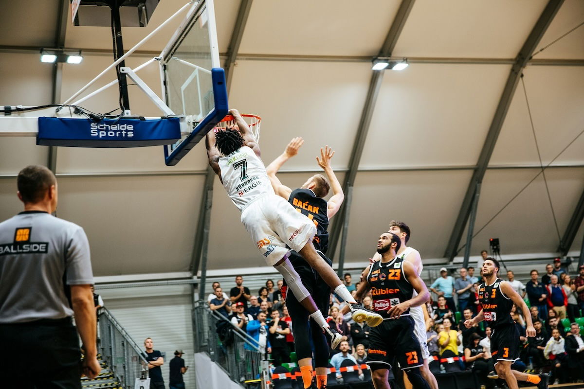 A player dunking a ball in a game with players and referee watching as an example of basketball photography