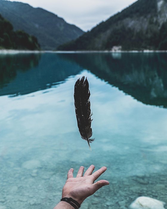 A feather levitating over an outstretched hand with a beautiful landscape in the background - beautiful photography principles