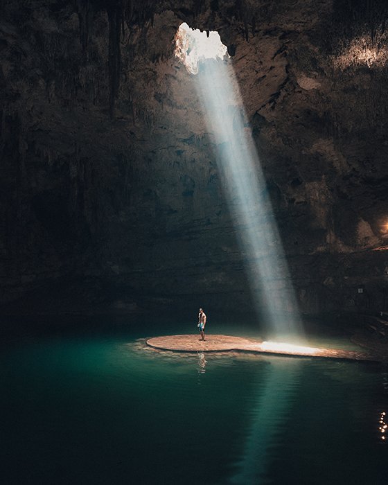 A beautiful photography shot of a person standing in a cave under a beam of light