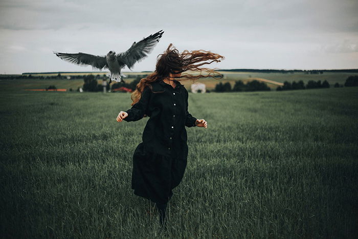 A conceptual dark portrait of a female model running away from a bird in a field - moody photography