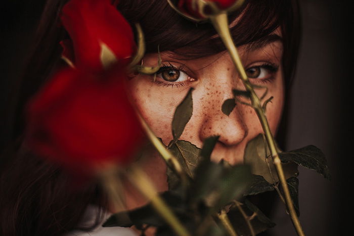 Atmospheric close up portrait of a moody female model with roses covering her face - examples of dark portraits