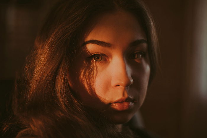 Atmospheric portrait of a moody female model looking straight to the camera in low light - examples of dark portraits