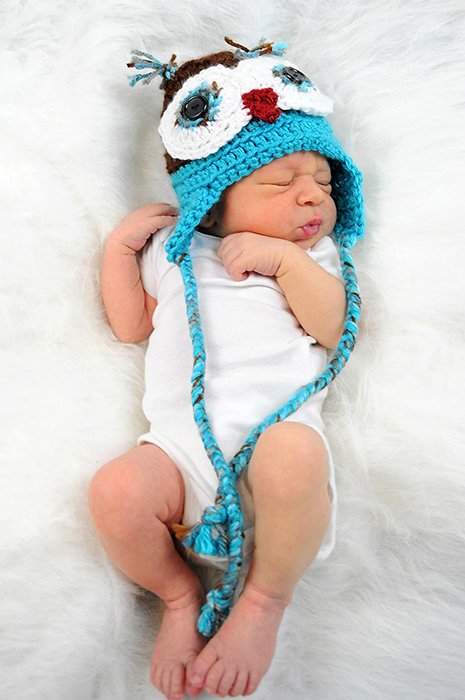 一个可爱的头顶婴儿的肖像，在一个白色的毯子上戴着新奇的帽子- diy新生儿摄影