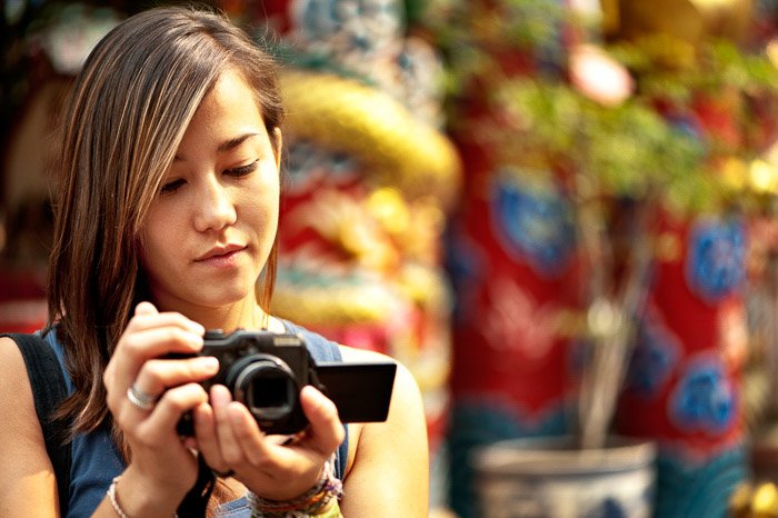 A female photographer holding a compact camera against a blurry background - grey market cameras