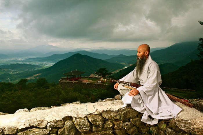 A monk sitting on a wallgazing off into the distance, with a beautiful mountainous landscape behind him - rule of space in photography