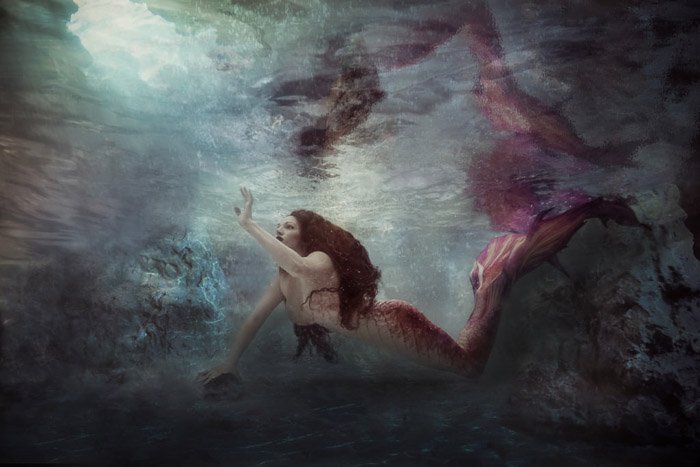 A surreal underwater portrait of a female model in mermaid tail posing underwater