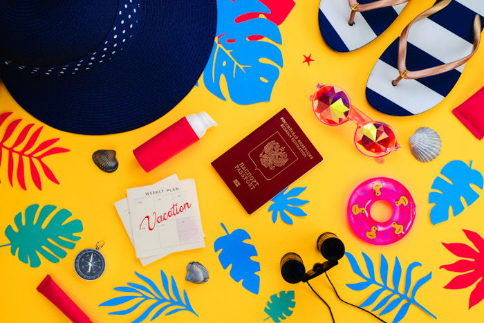 A summertime-themed flat lay including travel items on a yellow background 