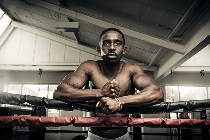 Atmospheric boxing photography of a fighter leaning against the ropes in a gym