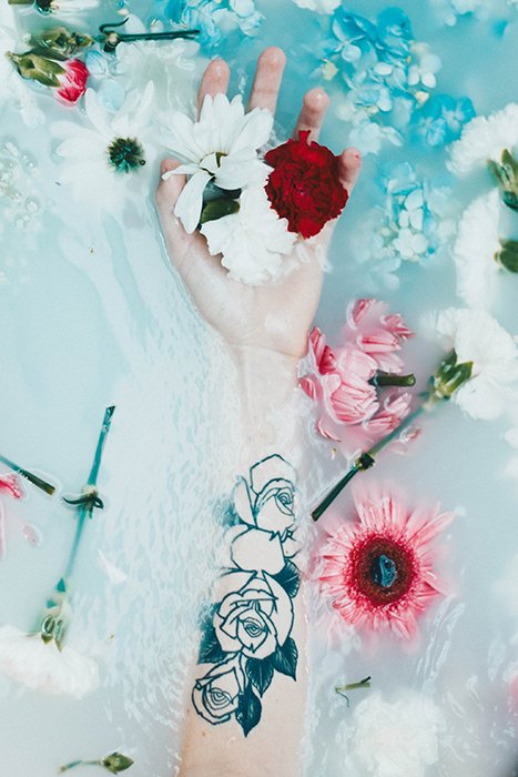 a tattooed arm and flowers in a milk bath