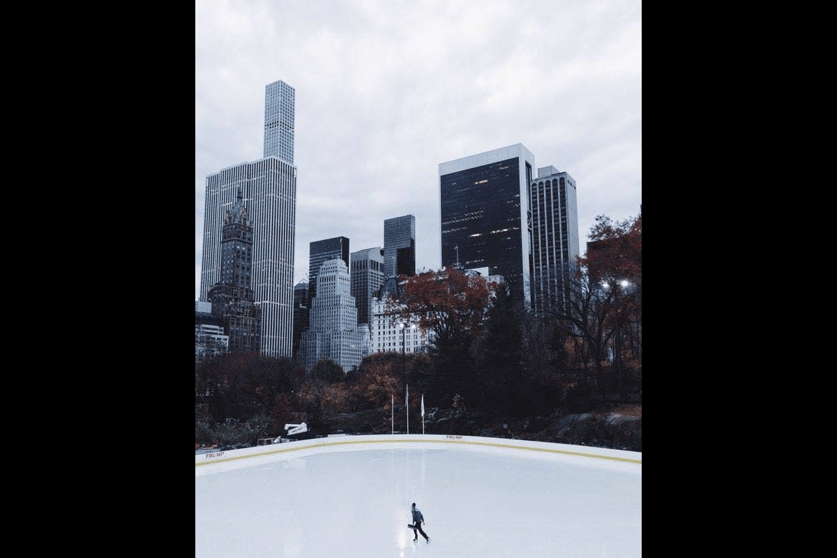 A skater on an outdoor rink with city buildings in the background