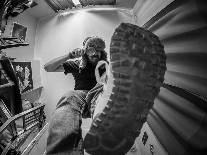 Humorous portrait of a man with a magnifying glass and pointing his shoe to the camera lens shot with a fisheye lens