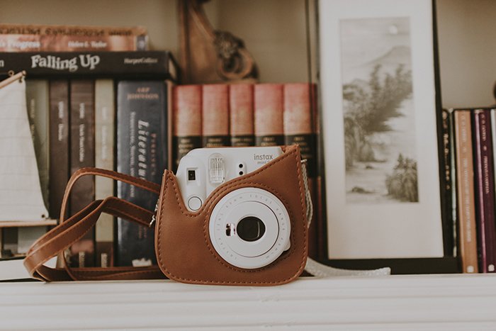 An instant camera in a case sitting on a shelf with books