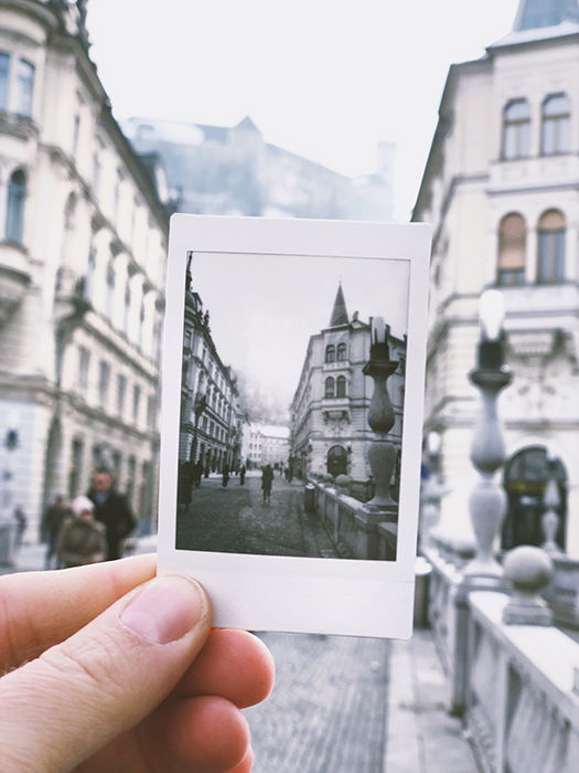 A person holding an instant photo of a cityscape within an actual cityscape