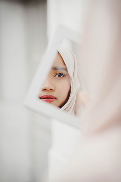 Striking portrait of a beautiful female model posing in a mirror for a makeup photography shoot