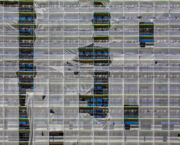 A multi windowed building covered by scaffolding and plastic