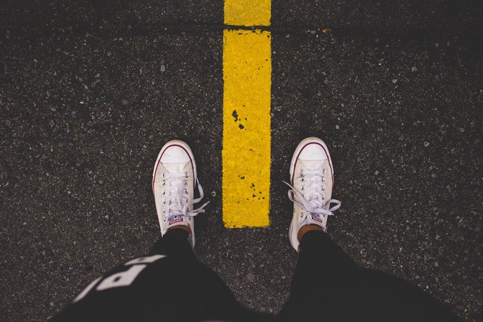 An overhead shot of a persons feet standing over a yellow line on the road