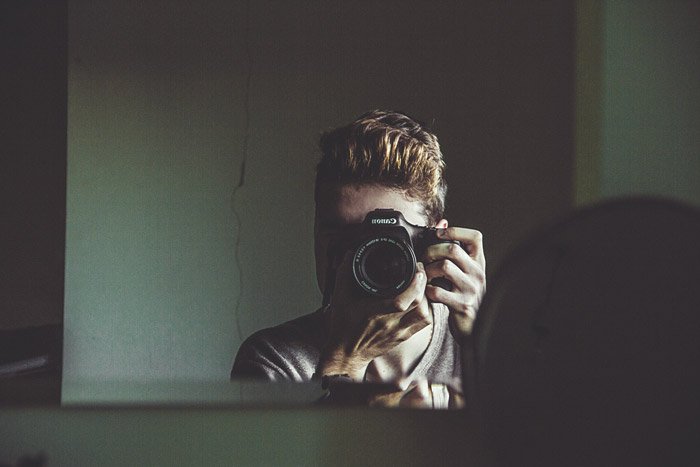 A male photographer talking a self portrait of himself through the mirror - photography themes