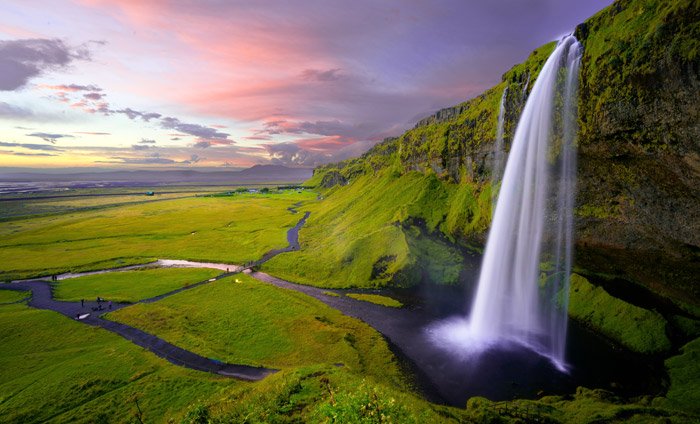 a luscious green mountainous landscape featuring a waterfall at evening - stunning landscape photos 
