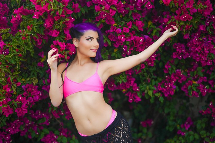 Atmospheric portrait of a female model posing outdoors in front of a pink flowered bush 