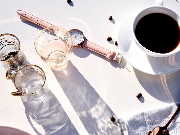 Overhead shot of coffee cup beside three small glasses and a watch