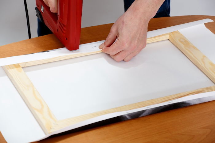 A person stapling a white cloth over a frame for a DIY photography lighting diffuser