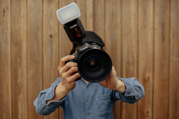 A photographer holding a dslr camera with a flash diffuser attached