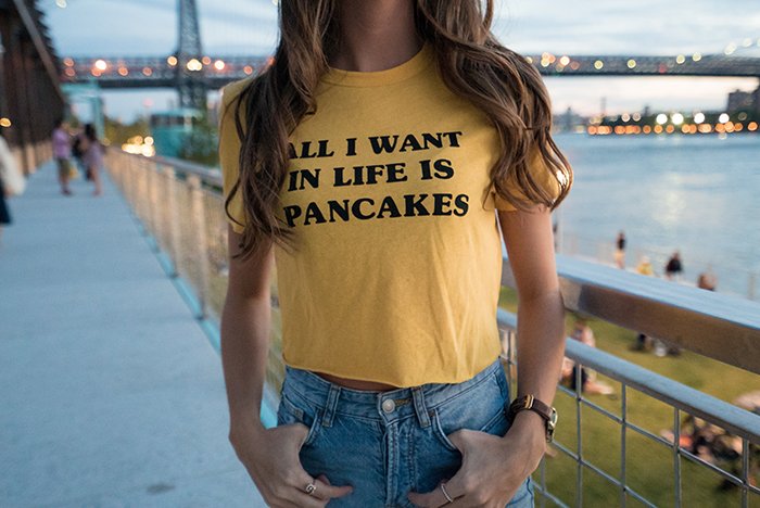 Un divertido retrato fotográfico de una chica con una camiseta que dice "todo lo que quiero en la vida en panqueques"