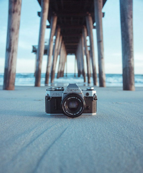 a canon film camera outdoors under a wooden pier