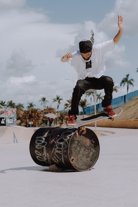A skateboarder performing a jump trick on a barrel in a skate park
