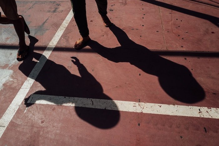 Two shadows on of people walking against red pavement with two white lines intersecting