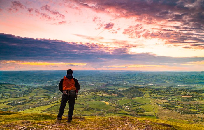 a hiker admiring the sunset from a luscious landscape - adventure photography skills