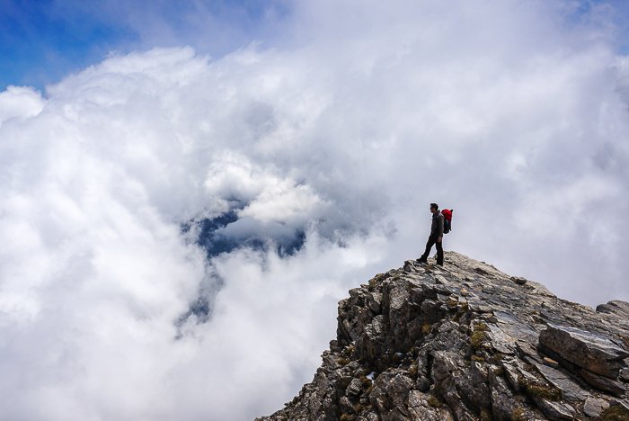 a hiker standing on the rocky peak of a mountainous landscape - adventure photography skills