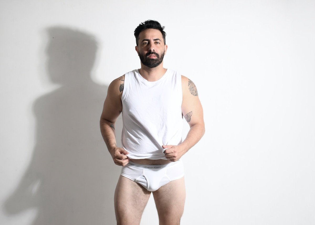 A male in a white tank top and underwear posing for a boudoir shoot against a white backdrop