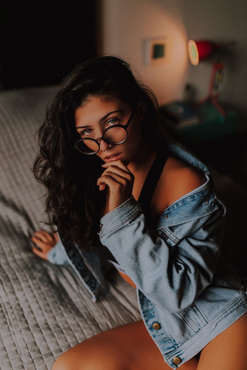 A female model in a denim jacket posing on a bed for a sexy boudoir shoot