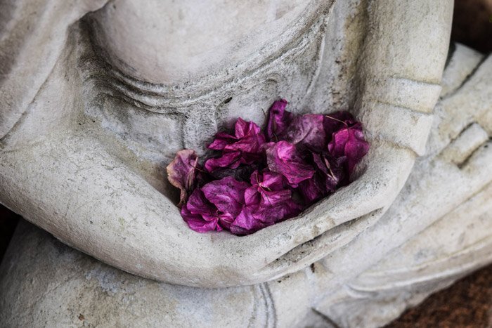 purple flowers collected in the arms of a stone statue - symbolism in photography