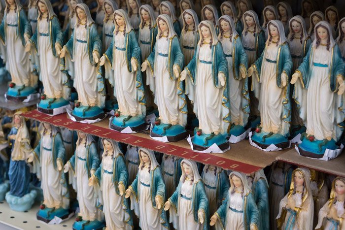 lines of holy Mary statues on a shelf - symbolism in photography