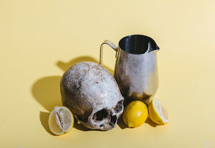 a still life featuring a skull, lemons and a vase on a pale yellow background - symbolism in photography